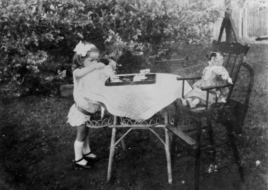 Una niña juega a servir el té a su muñeca en el jardín. La foto es de alrededor de 1915 y se guarda en The State Library of Queensland. 